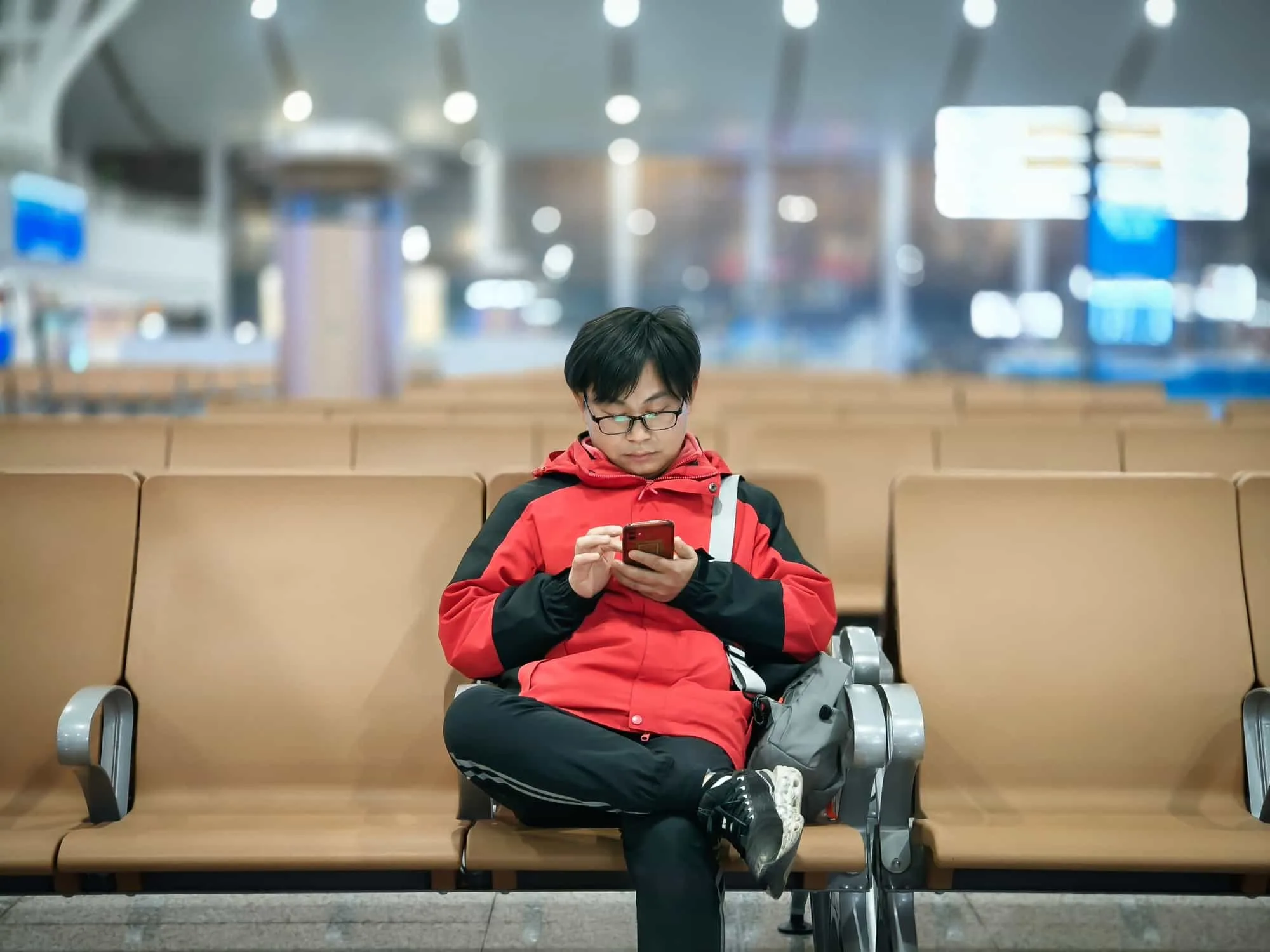一位男生坐在機場候機區椅子上，神情專注地思考要搭乘機場接送還是大眾運輸