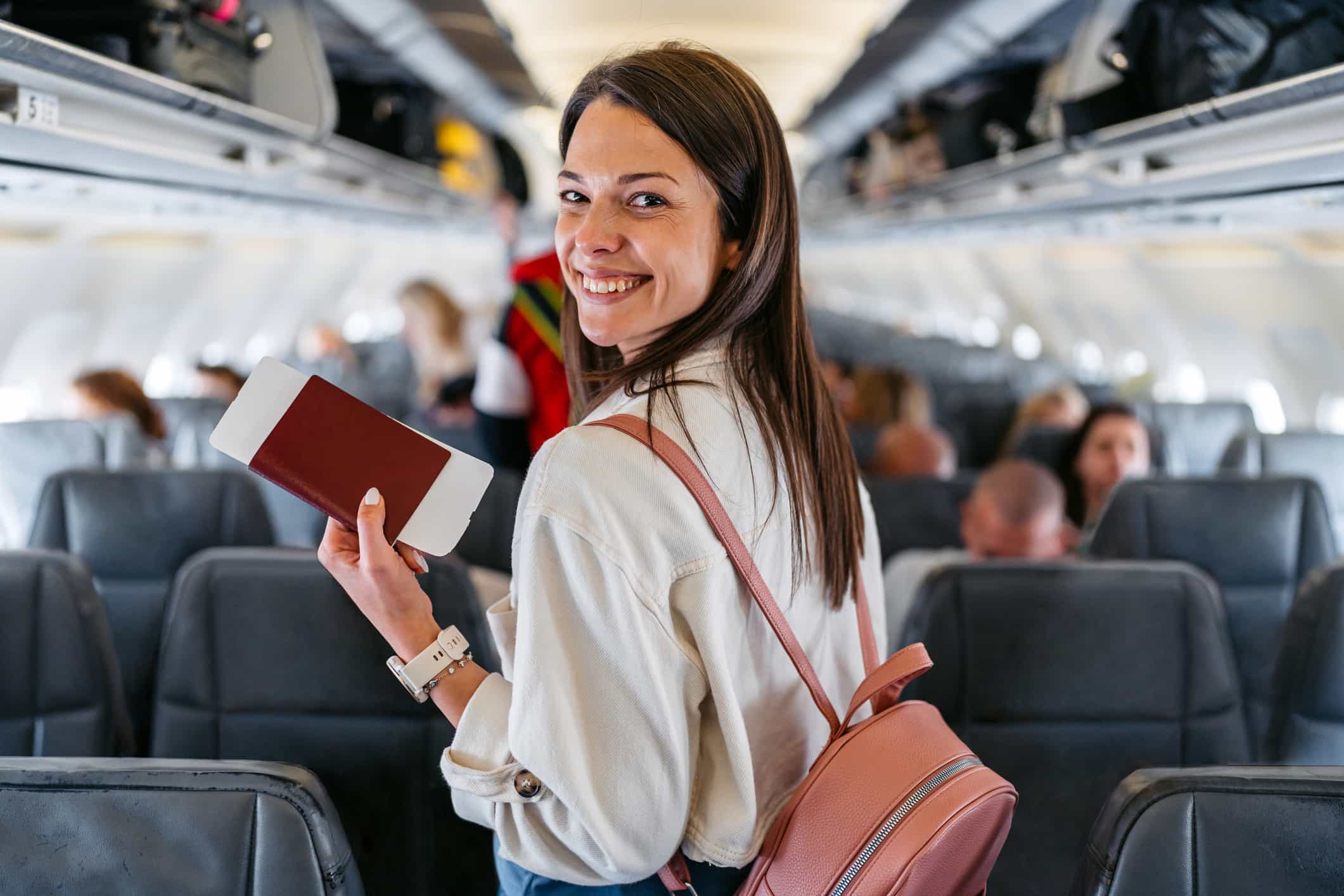 外國旅客在飛機上微笑迎接台灣之旅 - 機場接送首選、24H 專車預約、全台接送服務推薦|奔旅派車 - 機場接送首選、24H 專車預約、全台接送服務推薦|奔旅派車 一位外國女性旅客站在飛機機艙中,回頭露出燦爛笑容,象徵她對台灣旅程的期待與安心感。