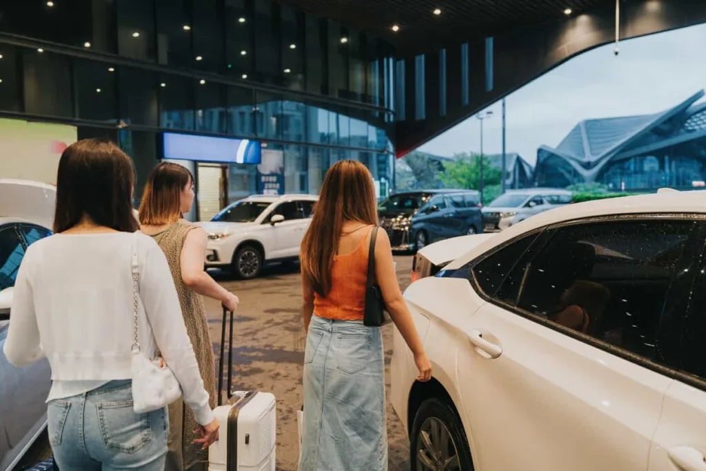 三位提著行李的女性在飯店門口準備搭車出發，呈現機場接送服務貼心銜接旅程的便利性。