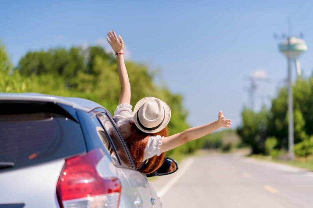女生從行駛中的車窗伸出雙手享受旅途自由，展現機場接送後自駕旅程的歡樂與放鬆。